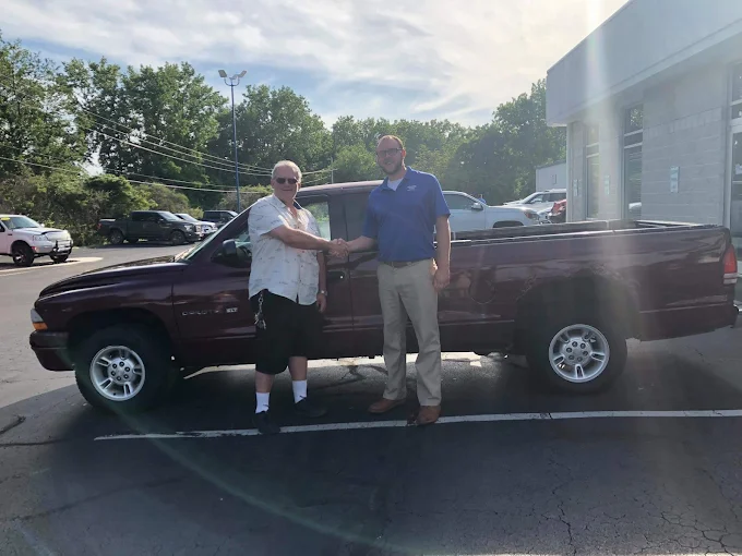 Two people beside a dark pickup truck at a Reineke dealership